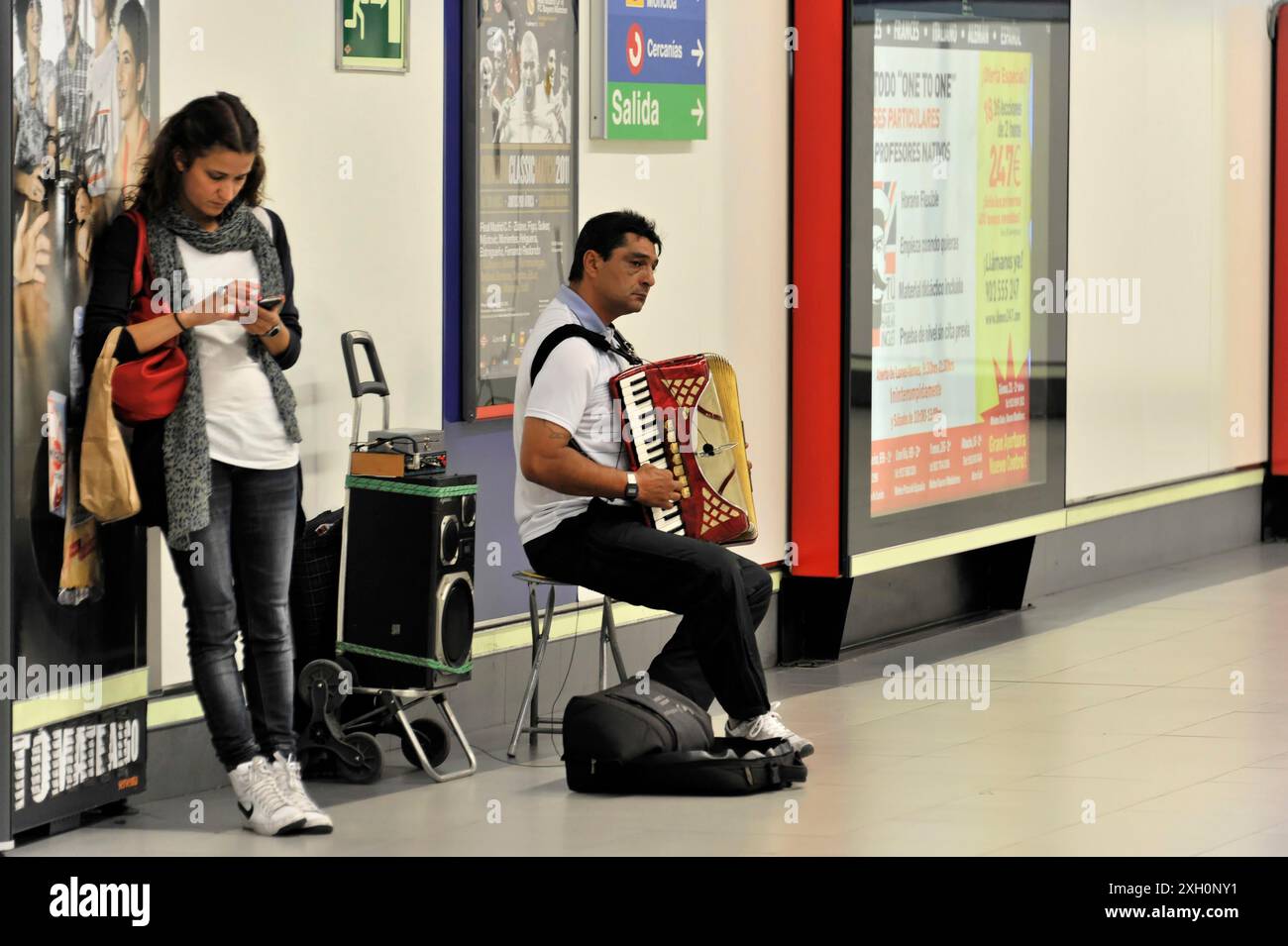 Madrid, Espagne, Europe, femme dans une station de métro utilisant son téléphone portable et un homme jouant de l'accordéon Banque D'Images