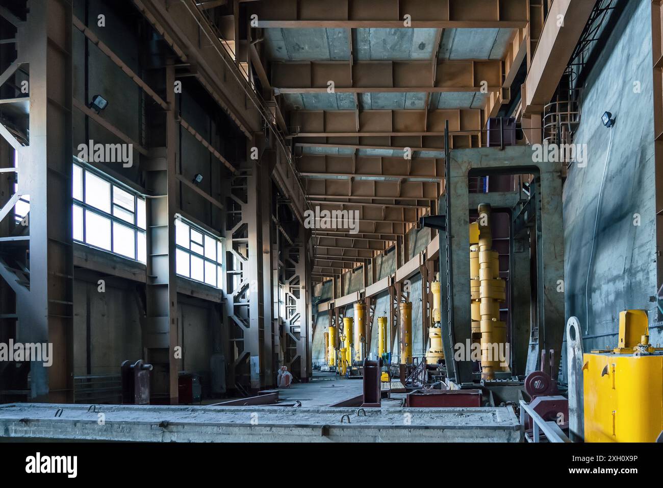 Grande installation industrielle avec machines et équipements lourds, avec de hauts plafonds et de grandes fenêtres laissant entrer la lumière naturelle. Banque D'Images