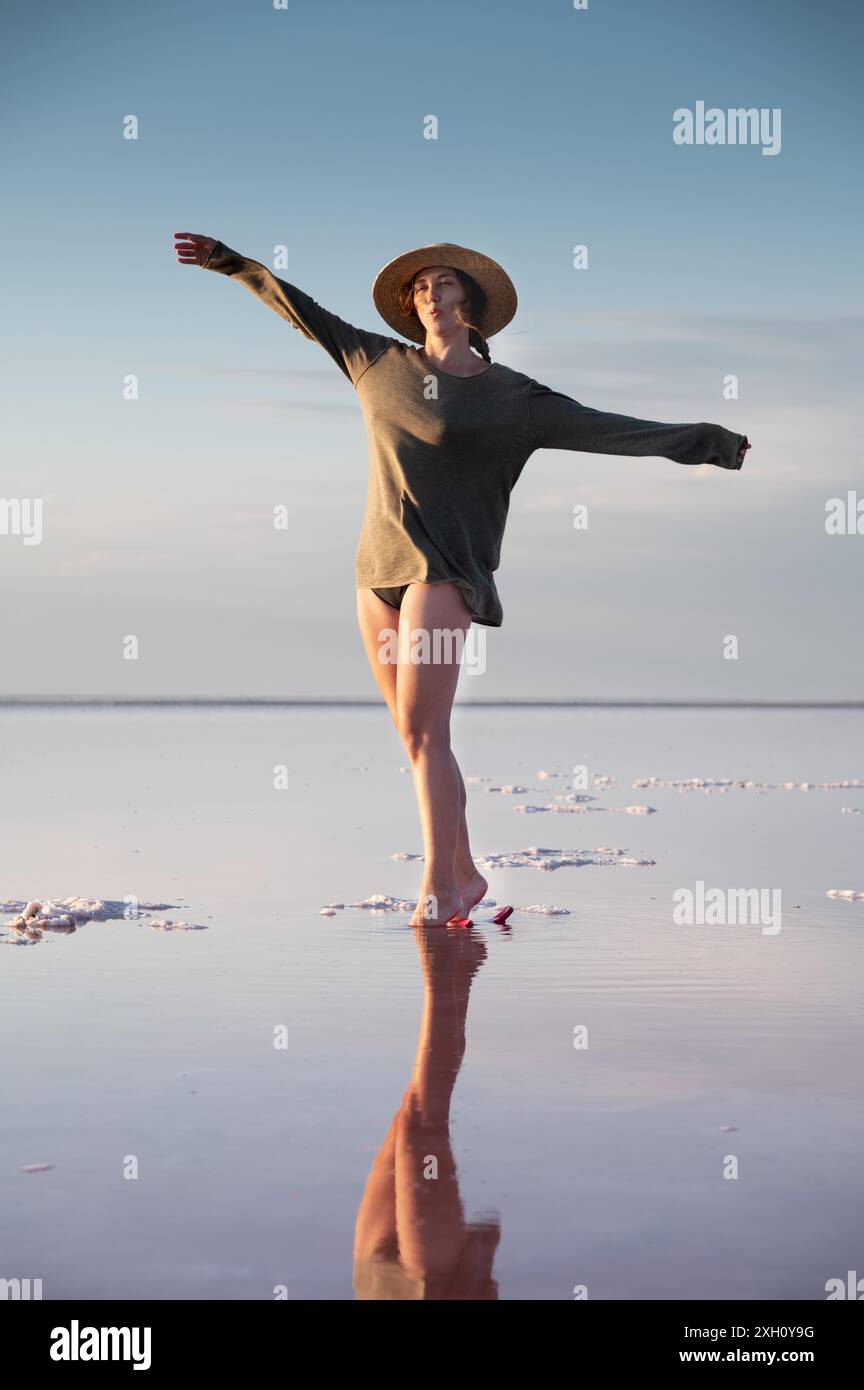 Vue en soirée sur le lac rose salé peu profond. Réflexion. Une jeune femme dans un chapeau marche sur l'eau et se reflète. Silence et harmonie. Bonheur Banque D'Images Vue en soirée sur le lac rose salé peu profond. Réflexion. Une jeune femme dans un chapeau marche sur l'eau et se reflète. Silence et harmonie. Bonheur Banque D'Images