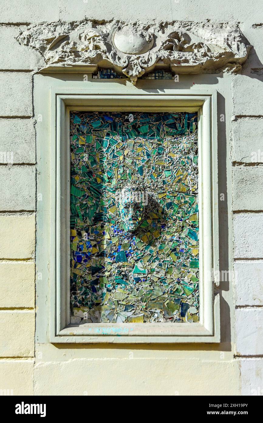 Illustration du visage en bas-relief faite de carreaux de couleur brisée et de verre dans une ancienne ouverture de fenêtre - Paris 75004, France. Banque D'Images