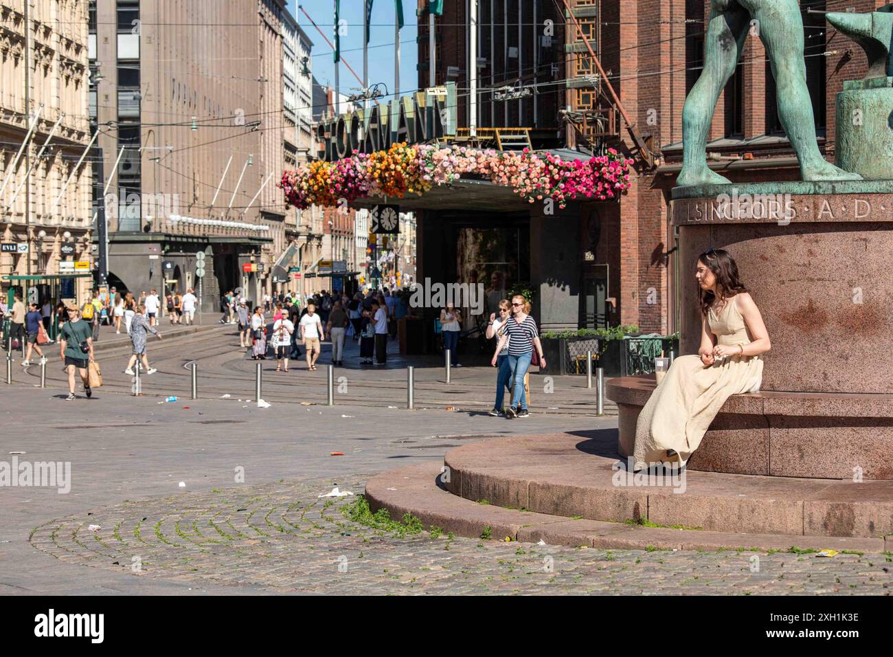 Jeune femme en vêtements d'été assise sur un piédestal de sculpture dans la zone piétonne Aleksanterinkatu dans le district de Kluuvi à Helsinki, Finlande Banque D'Images