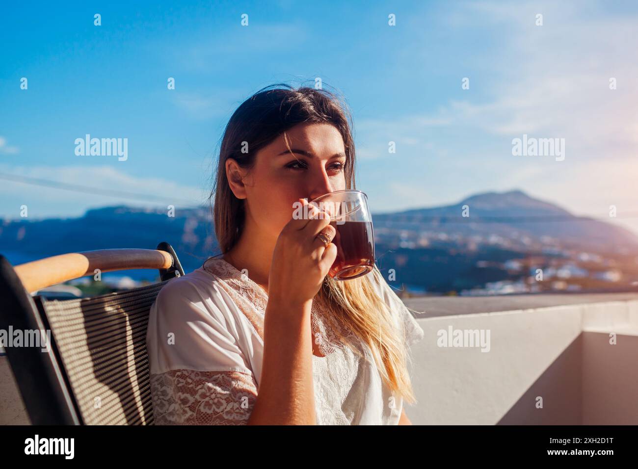 Femme se relaxant sur la terrasse de l'hôtel buvant le café du matin profitant du paysage de montagne. Petit déjeuner avec vue. Vacances d'été Banque D'Images