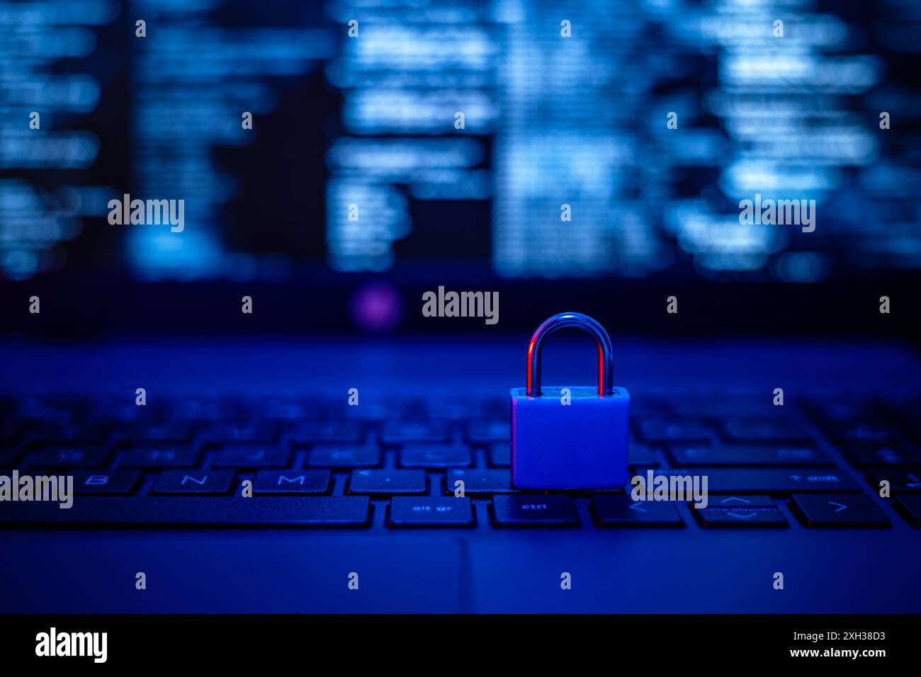 Un cadenas bleu repose sur un clavier d'ordinateur portable, éclairé par une lueur bleue. L'écran affiche un code flou, mettant l'accent sur la sécurité des données. Banque D'Images