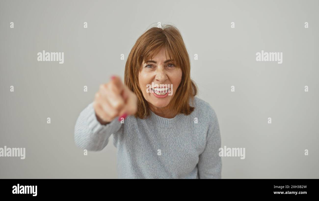 Femme d'âge moyen pointant avec colère la caméra sur un fond blanc, démontrant la frustration ou la confrontation. Banque D'Images