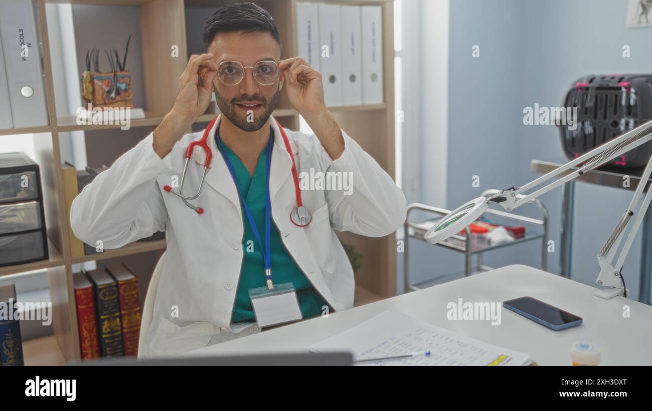 Vétérinaire masculin hispanique dans une clinique hospitalière ajustant des lunettes avec du matériel médical en arrière-plan. Banque D'Images