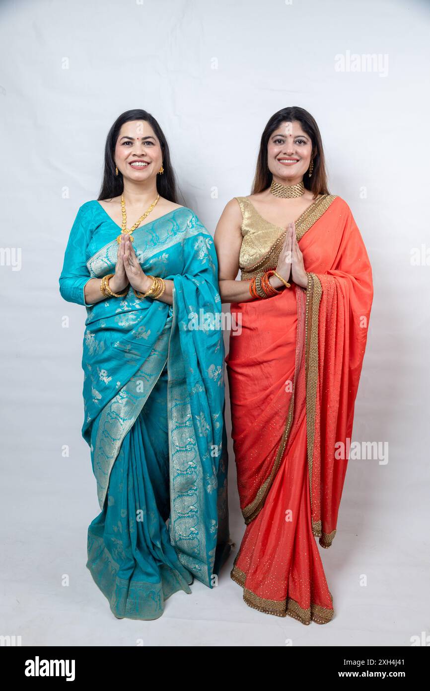 Deux femmes indiennes heureuses saluant, joignent les mains font namaste debout dans le saree, isolé sur fond blanc. Culture de l'inde. Banque D'Images