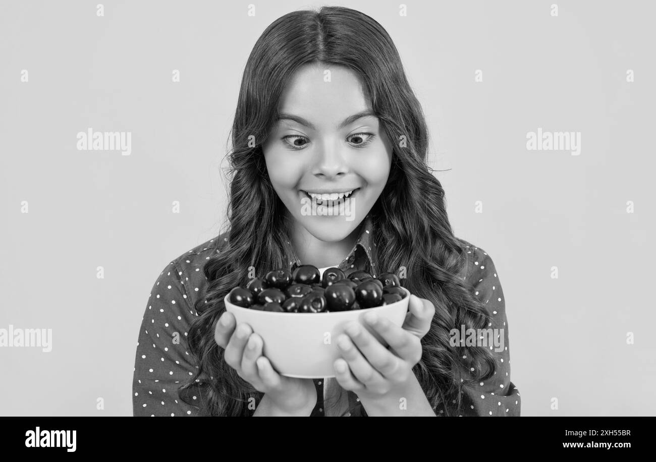 une jeune fille surprise tient un bol de cerise sur fond jaune Banque D'Images