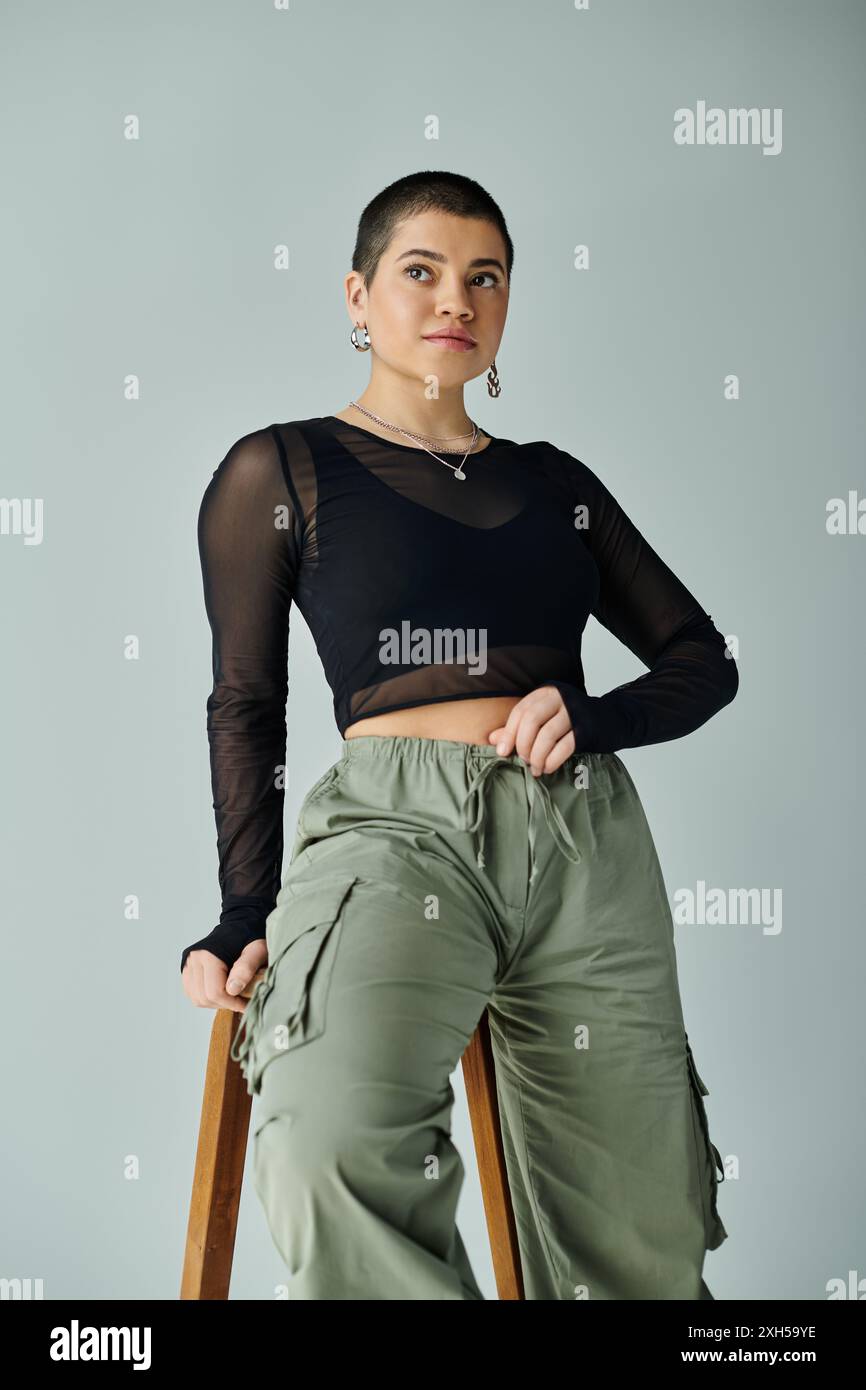Jeune femme aux cheveux courts dans une tenue décontractée élégante assise sur une chaise, les mains sur les hanches, exsudant confiance et affirmation de soi. Banque D'Images