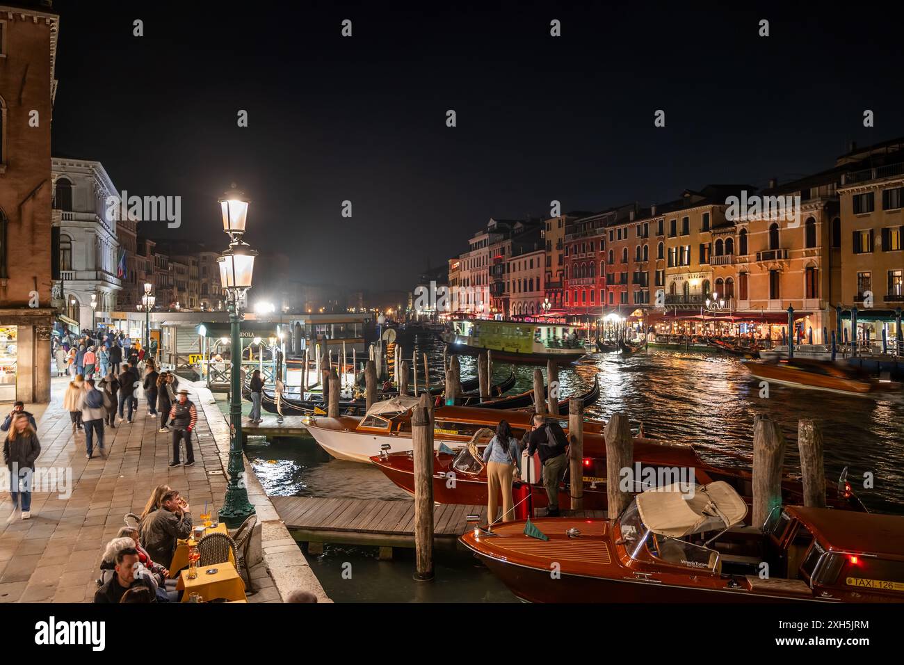 Le Grand canal dans la ville de Venise la nuit, Italie. Front de mer dynamique près du pont du Rialto avec des gondoles, des gens, de l'eau scintillante et la ligne d'horizon de San ma Banque D'Images