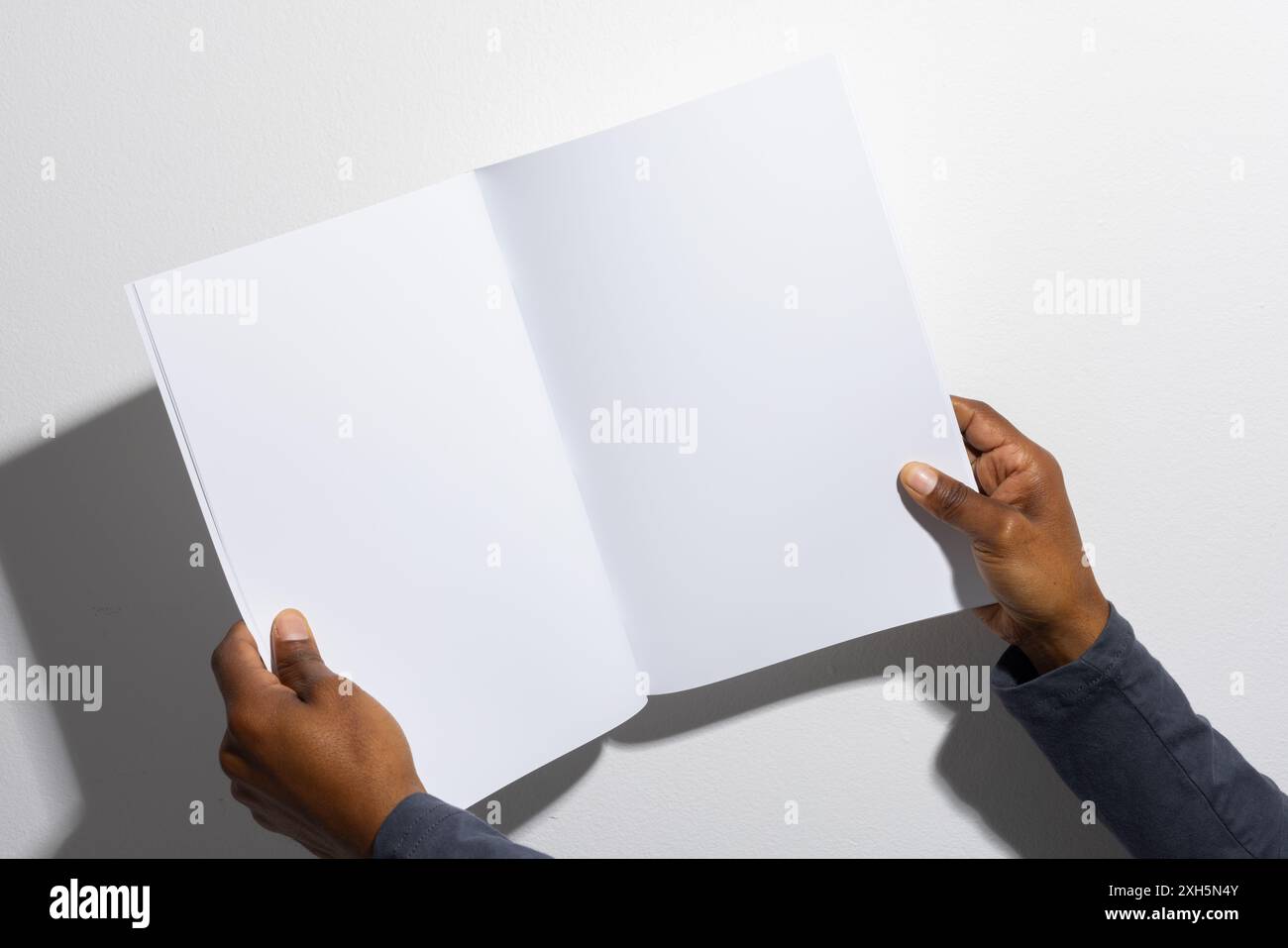 Mains d'un homme afro-américain tenant un magazine vierge ouvert, avec espace de copie. Idéal pour la présentation de travaux de conception ou de mise en page d'impression dans un s professionnel Banque D'Images