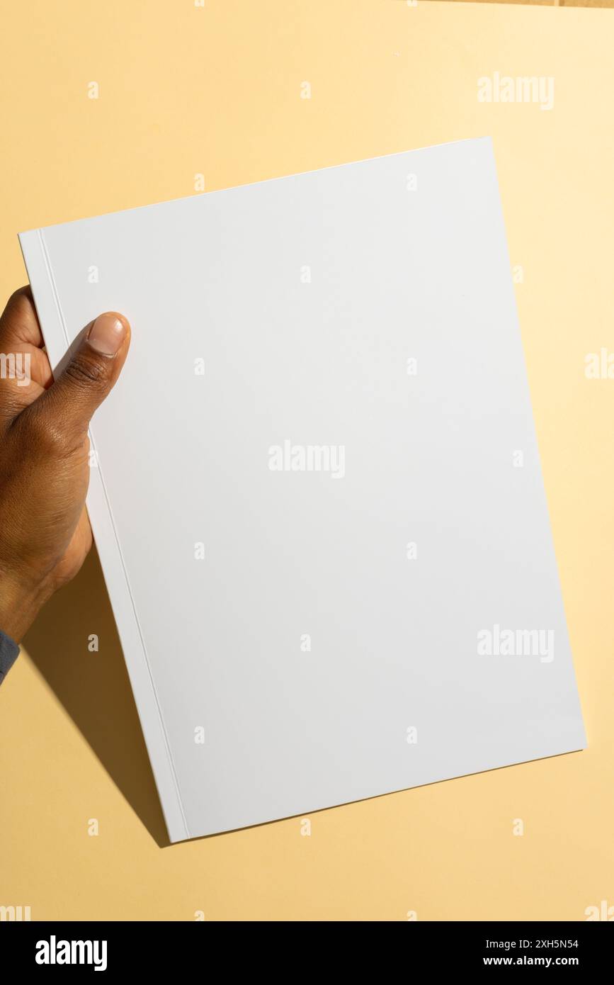 Homme biracial tenant un papier blanc vierge, avec espace de copie. Idéal pour les présentations ou la publicité dans un contexte propre et simple. Banque D'Images