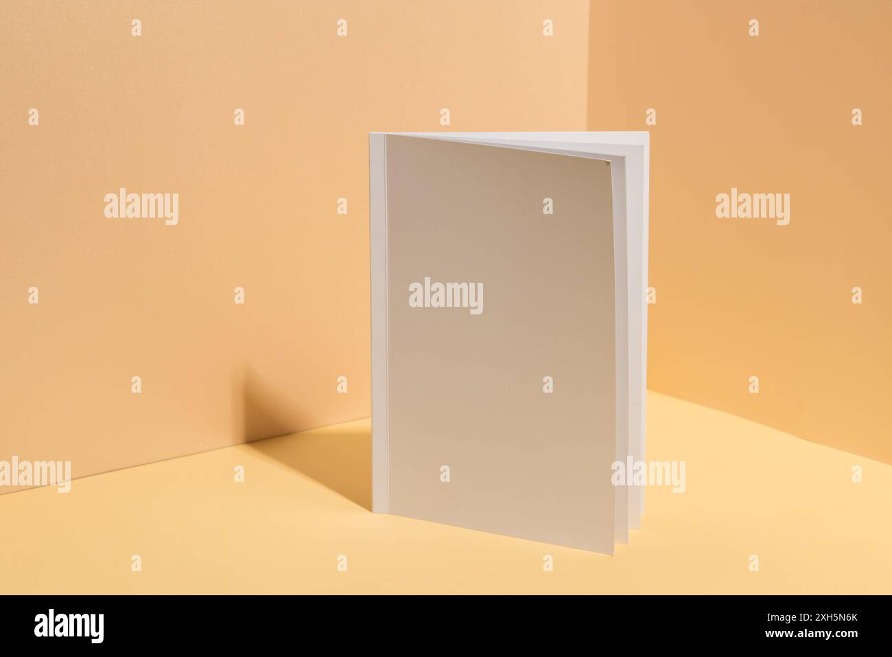 Un livre blanc vierge se tient ouvert sur un fond beige avec espace de copie. Idéal pour mettre en valeur les conceptions de couverture, l'image souligne le potentiel de Banque D'Images