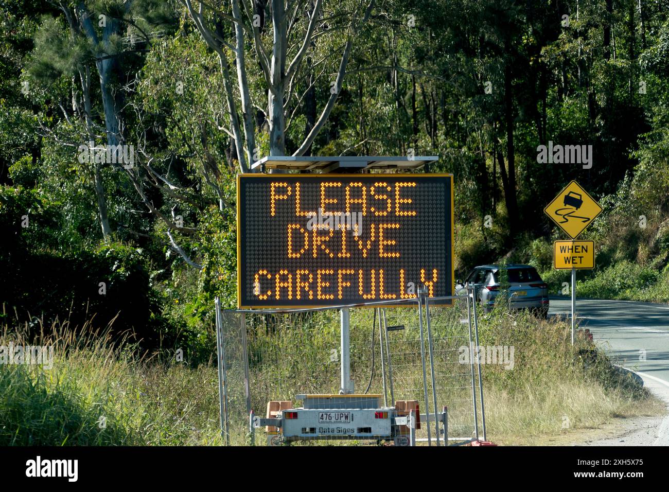 Polis panneau lumineux « Please Drive prudemment » à côté d'une route très fréquentée dans le Queensland, en Australie, dans une zone boisée verdoyante près de Gold Coast. Banque D'Images