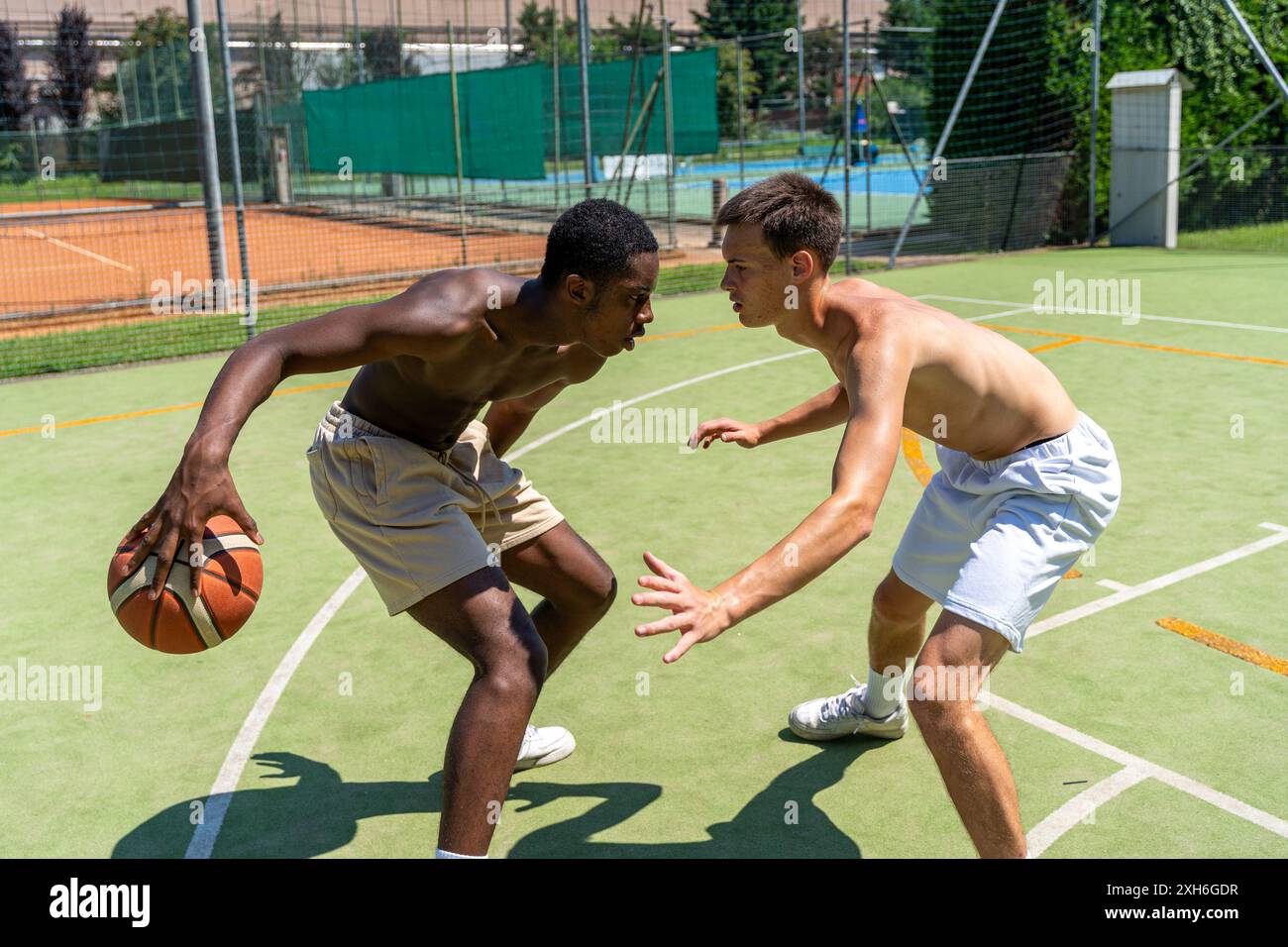 deux jeunes athlètes multiethniques joueurs de basket-ball en action se font face sur le terrain de jeu en gazon artificiel lors d'une journée d'été ensoleillée à l'extérieur Banque D'Images