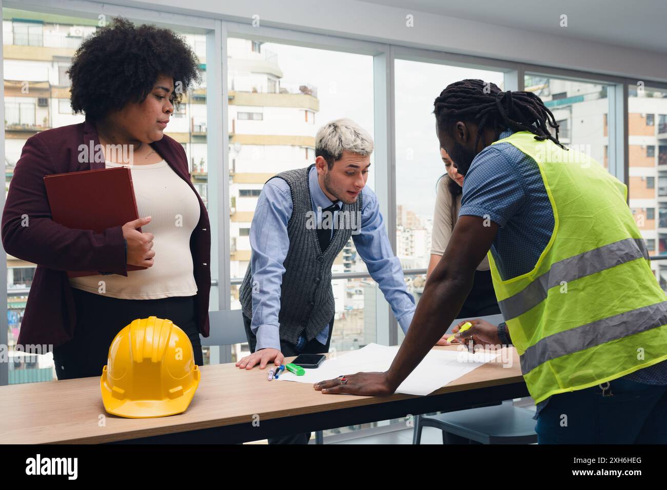 Les gens réunis dans le conseil d'administration, examinent les plans de construction avec l'ingénieur, deux hommes et une femme debout autour de la table dans le bureau, sont travail Banque D'Images