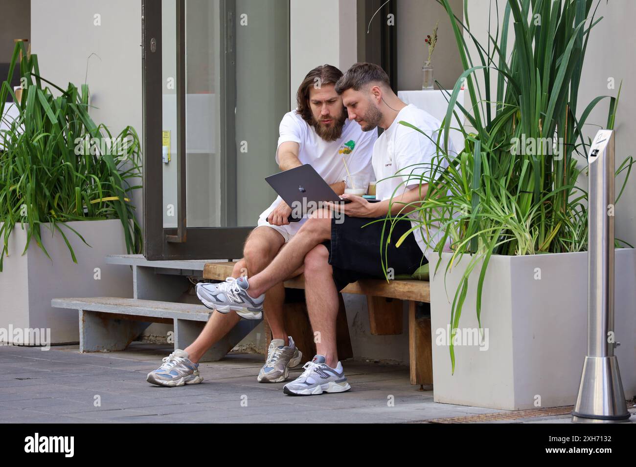 Deux hommes assis avec un ordinateur portable dans un café de rue. Vie en ville d'été, travail d'équipe Banque D'Images