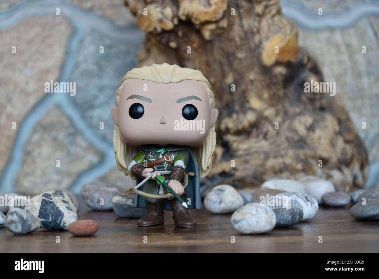 Funko Pop figurine d'action vinyle de elfe Legolas du film fantastique le Seigneur des anneaux. Guerrier en armure tenant l'arc et la flèche. Vieil arbre, pierres. Banque D'Images