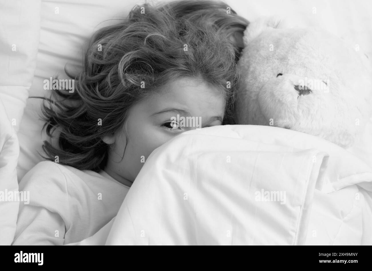 Réveil matinal petit enfant avec jouet ours en peluche dans le lit. Un enfant se réveille dans la chambre. Banque D'Images