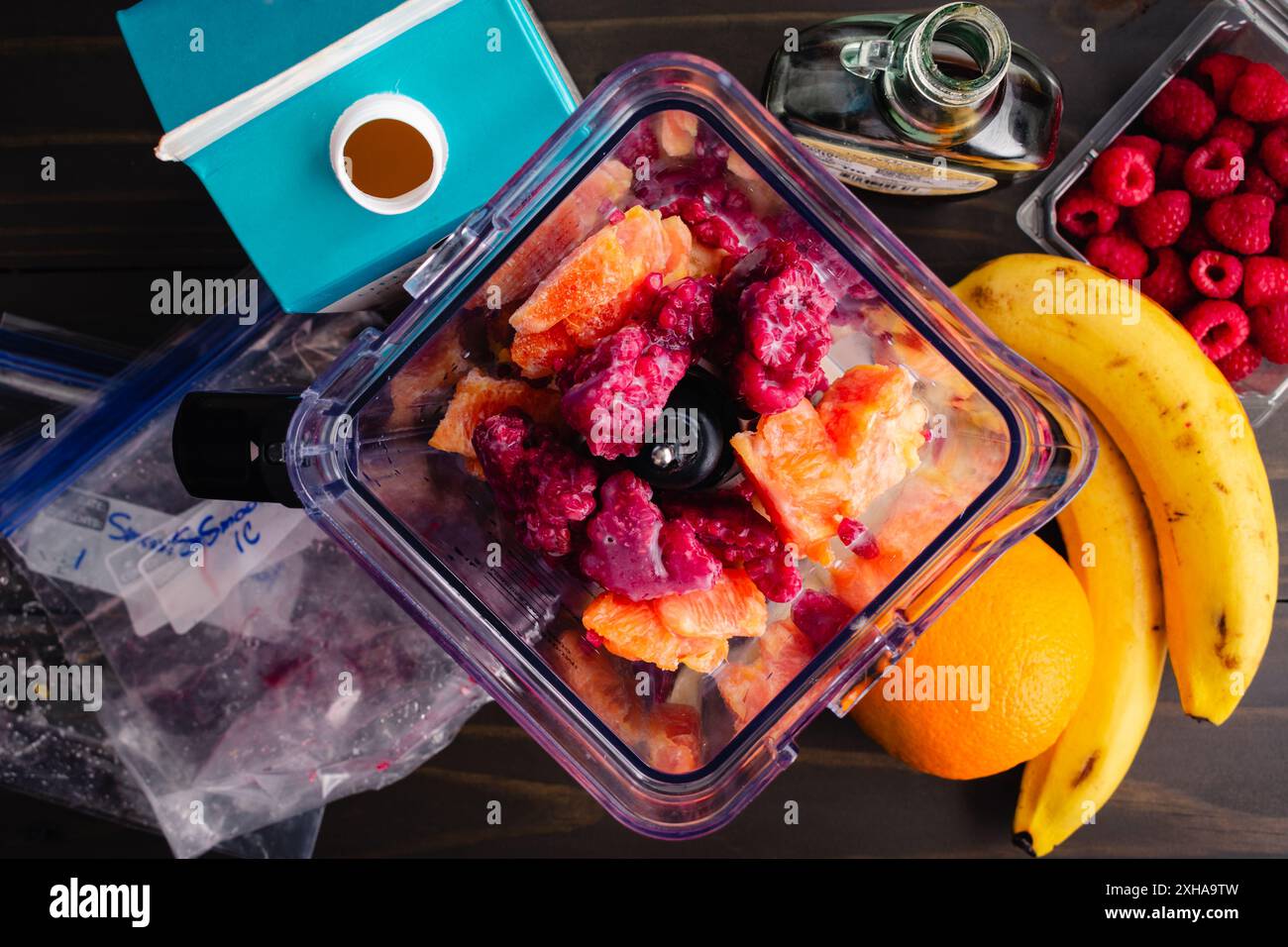 Framboise Orange Smoothie Bowl ingrédients dans un mélangeur : framboises surgelées non mélangées, orange et banane avec lait d'amande et sirop d'érable Banque D'Images