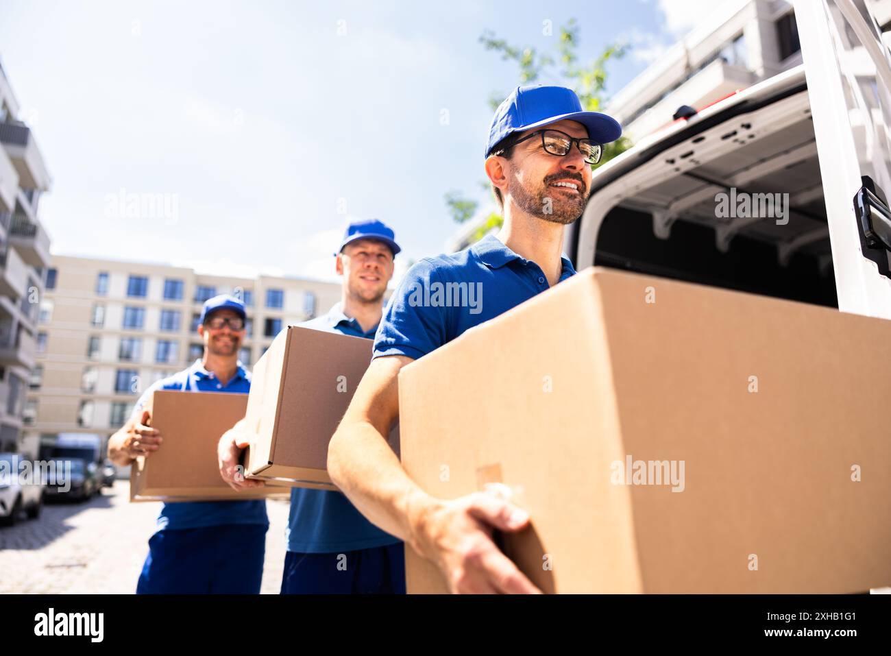 Livreurs travaillant ensemble pour transporter une boîte en carton devant un camion. Déménageurs professionnels fournissant des services de messagerie efficaces. Banque D'Images