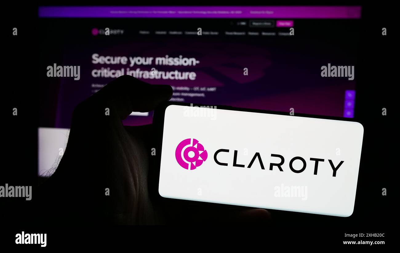 Personne tenant le téléphone portable avec le logo de la société de cybersécurité Claroty Ltd en face de la page Web de l'entreprise. Concentrez-vous sur l'affichage du téléphone. Banque D'Images
