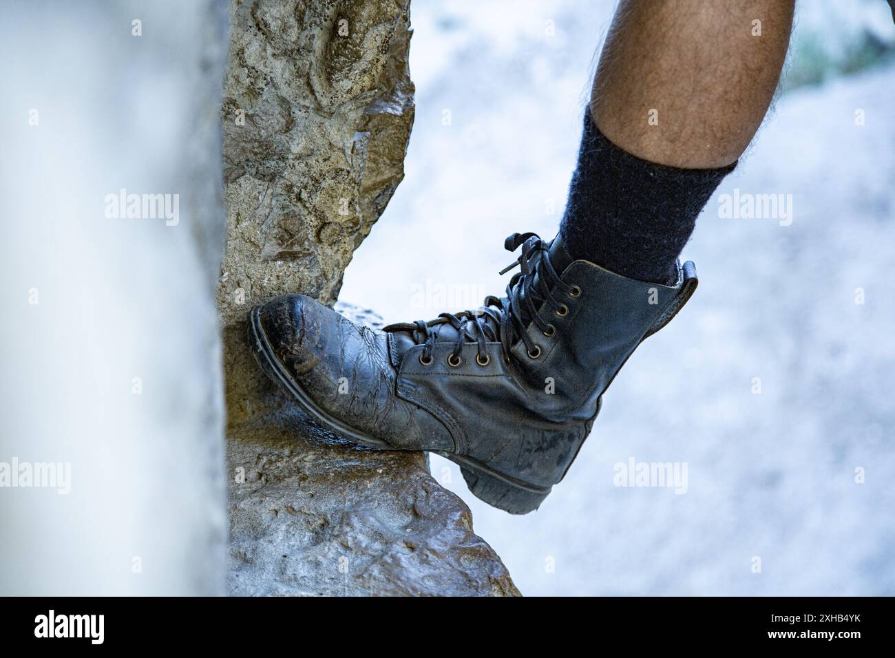 Gros plan d'un pied masculin en vieilles bottes en cuir et chaussettes hautes en laine reposant sur un rebord en pierre dans le mur. Archéologie. Étudiez. Voyage. Banque D'Images
