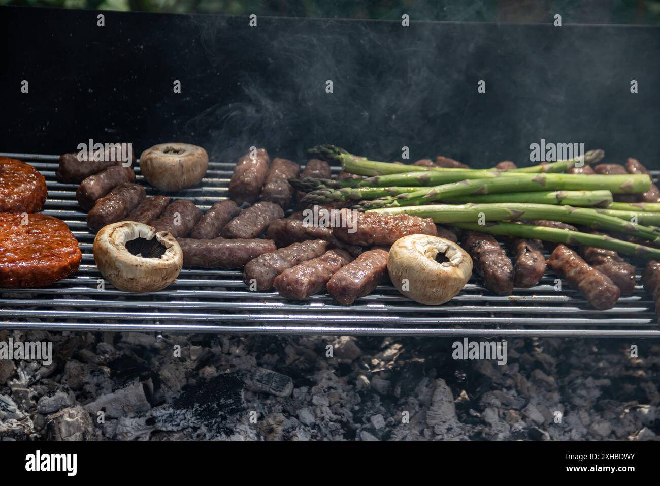 Champignons, asperges, Cevapi, Pljeskavica et poulet grésillent sur le barbecue, entouré de fumée, mêlant saveurs fumées et épices traditionnelles Banque D'Images