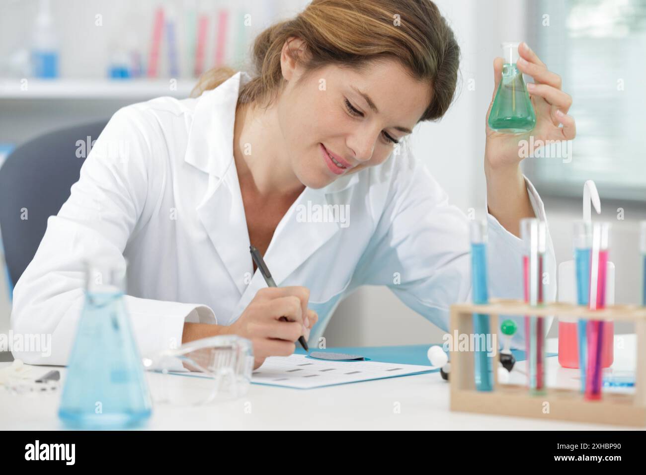 scientifique femme souriante avec un tube à essai écrivant des notes Banque D'Images