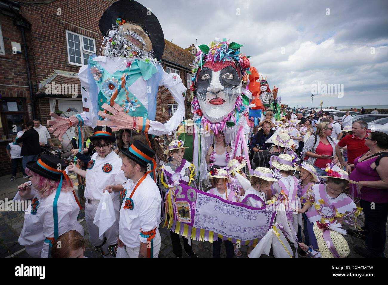 Folkestone, Kent, Royaume-Uni. 13 juillet 2024. Défilé annuel du Charivari Day. Folklore britannique et traditions rituelles sont le thème de la saisissante parade du carnaval de cette année. Des sculptures massives de tête ornent les épaules des jeunes locaux avec des enfants de l'école primaire à travers le district habillant aux couleurs du thème de l'année. Marchant du stade, en passant par la ville jusqu’au kiosque à musique Leas, le Charivari Day reste la plus grande tradition coutumière de Folkestone depuis 1997 et attire des centaines de spectateurs dans la ville portuaire en bord de mer. Crédit : Guy Corbishley/Alamy Live News Banque D'Images