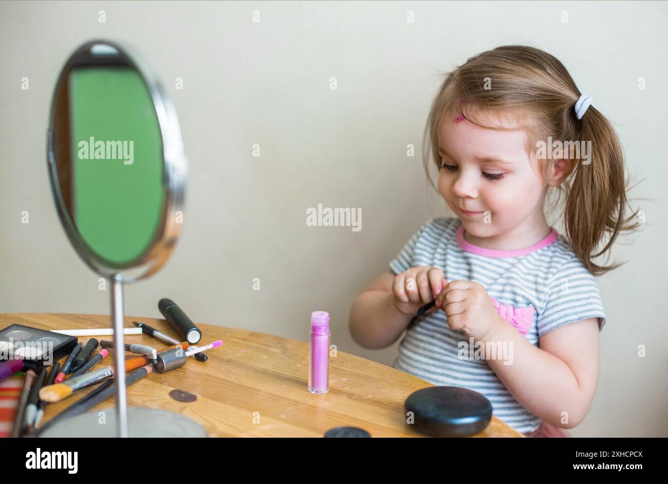 Adorable petite fille jouant avec les cosmétiques et se maquillant tout en se regardant dans le miroir Banque D'Images