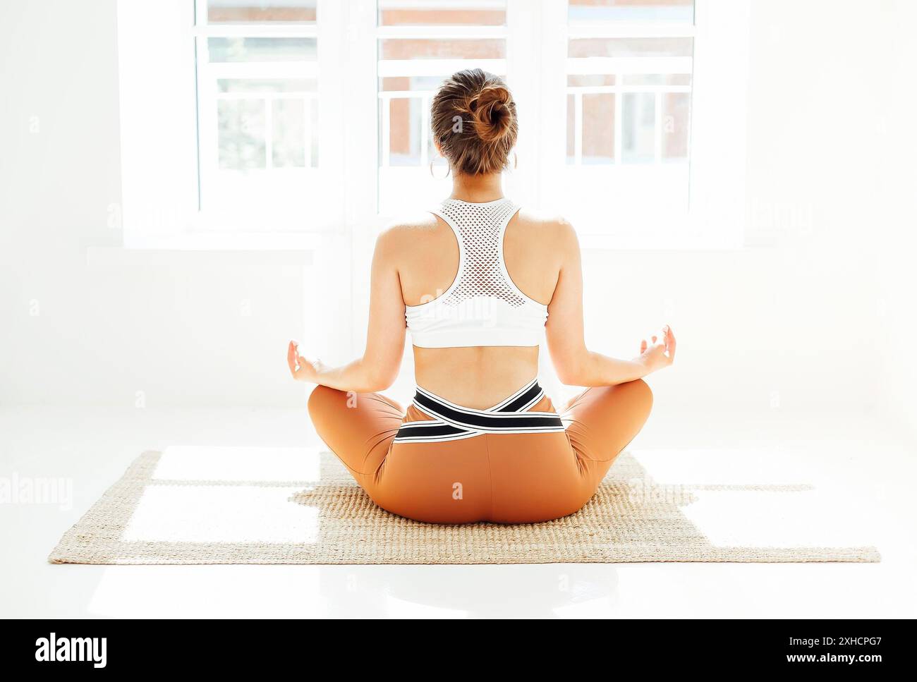 Vue arrière de la femme méconnue dans les vêtements de sport assis avec les jambes croisées et les mains mudra sur le tapis et faisant du yoga tout en pratiquant la pleine conscience Banque D'Images