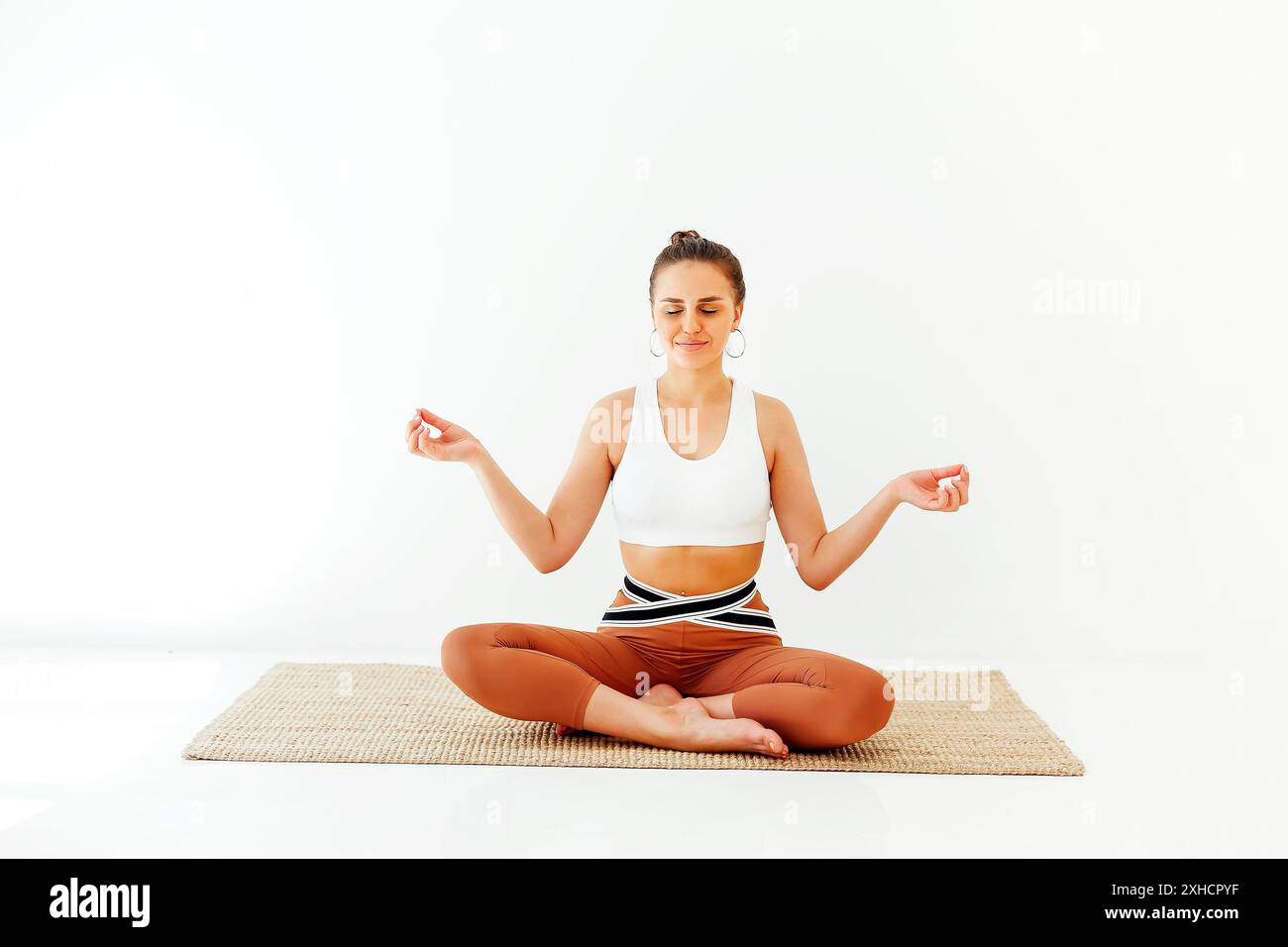 Jeune femme de sport assise avec des jambes croisées et des mains mudra sur le tapis et faisant du yoga tout en pratiquant la pleine conscience Banque D'Images