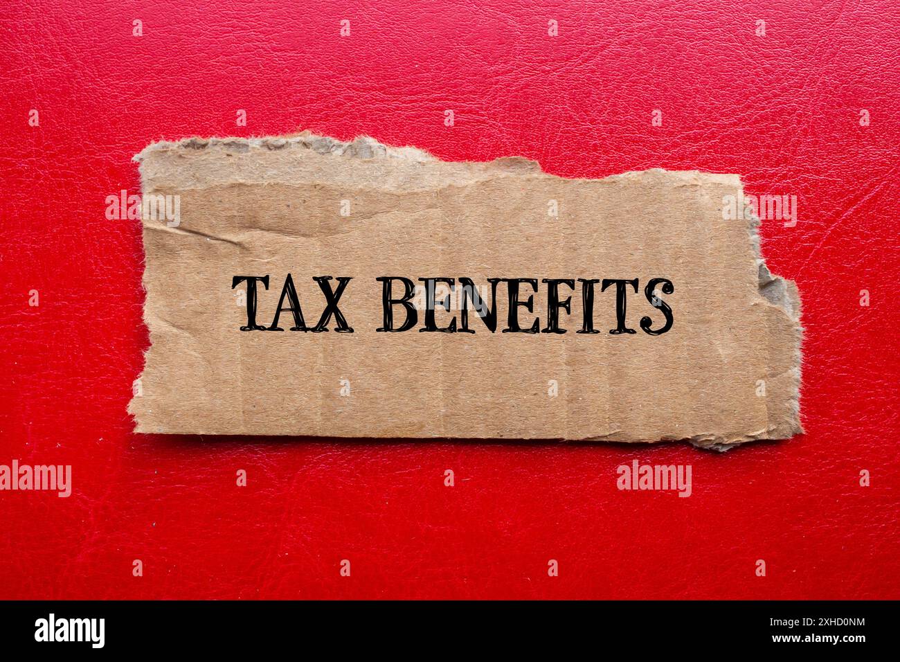 Mots sur les avantages fiscaux écrits sur un morceau de papier de carton déchiré avec un fond rouge. Symbole d'avantages fiscaux conceptuels. Copier l'espace. Banque D'Images
