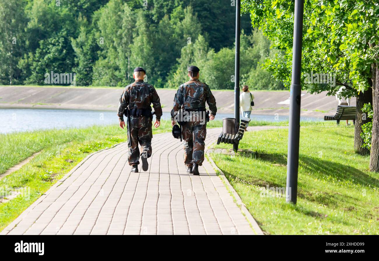 Deux policiers de sexe masculin avec des uniformes noirs vus de derrière marchant dans le parc de la ville et luttant contre la criminalité Banque D'Images