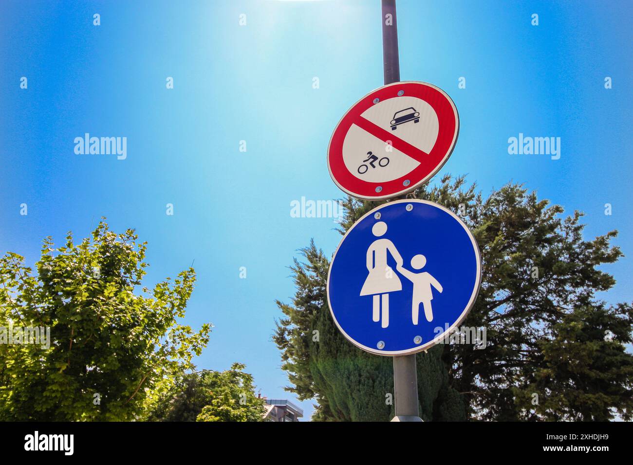 Un panneau bleu pour piétons et un panneau rouge d'interdiction de véhicule ou de bicyclette, montés sur un poteau de lampadaire contre un ciel bleu vif d'été. Banque D'Images