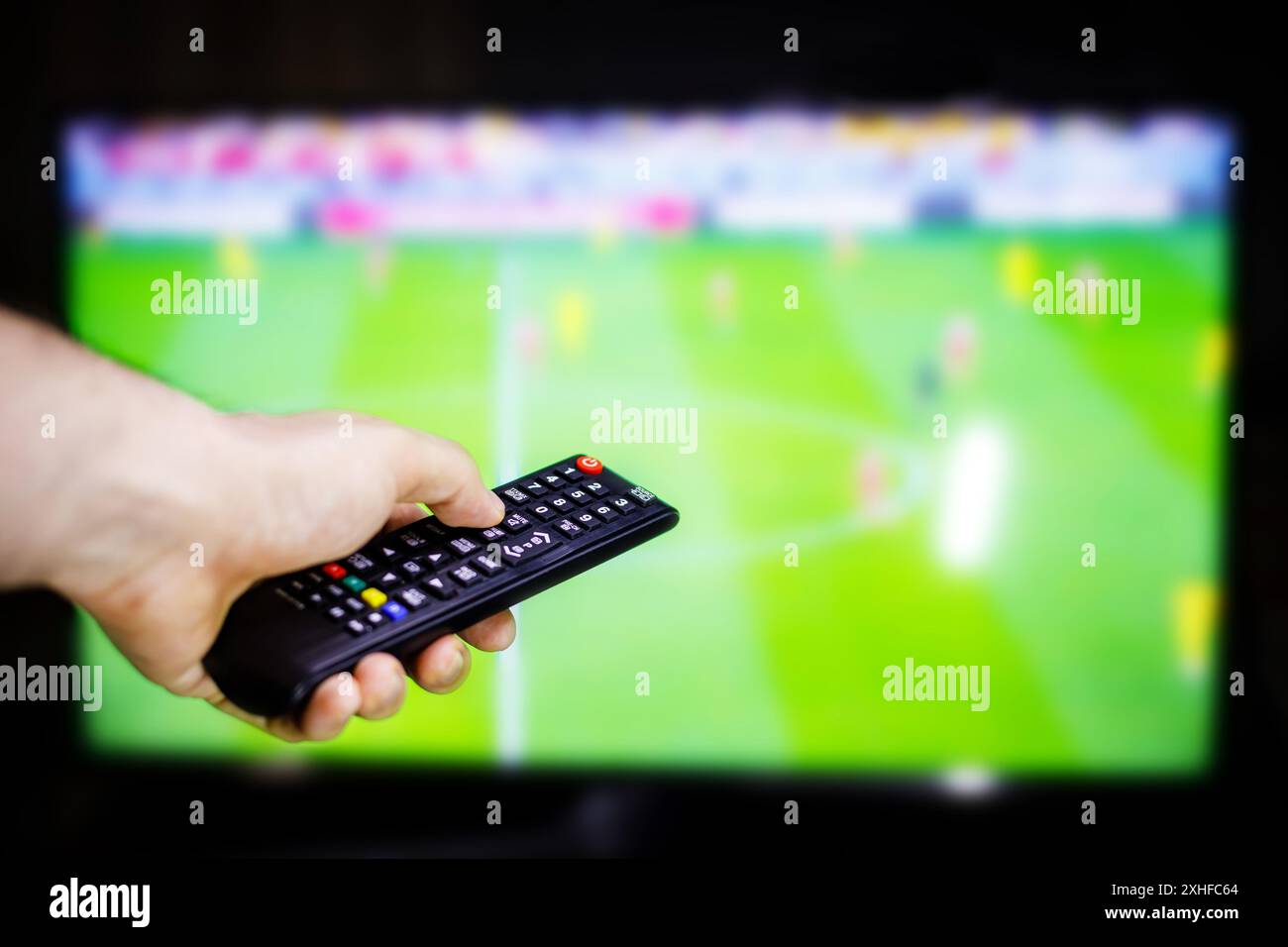 Une main tient une télécommande devant un écran de télévision montrant un match de football. Banque D'Images