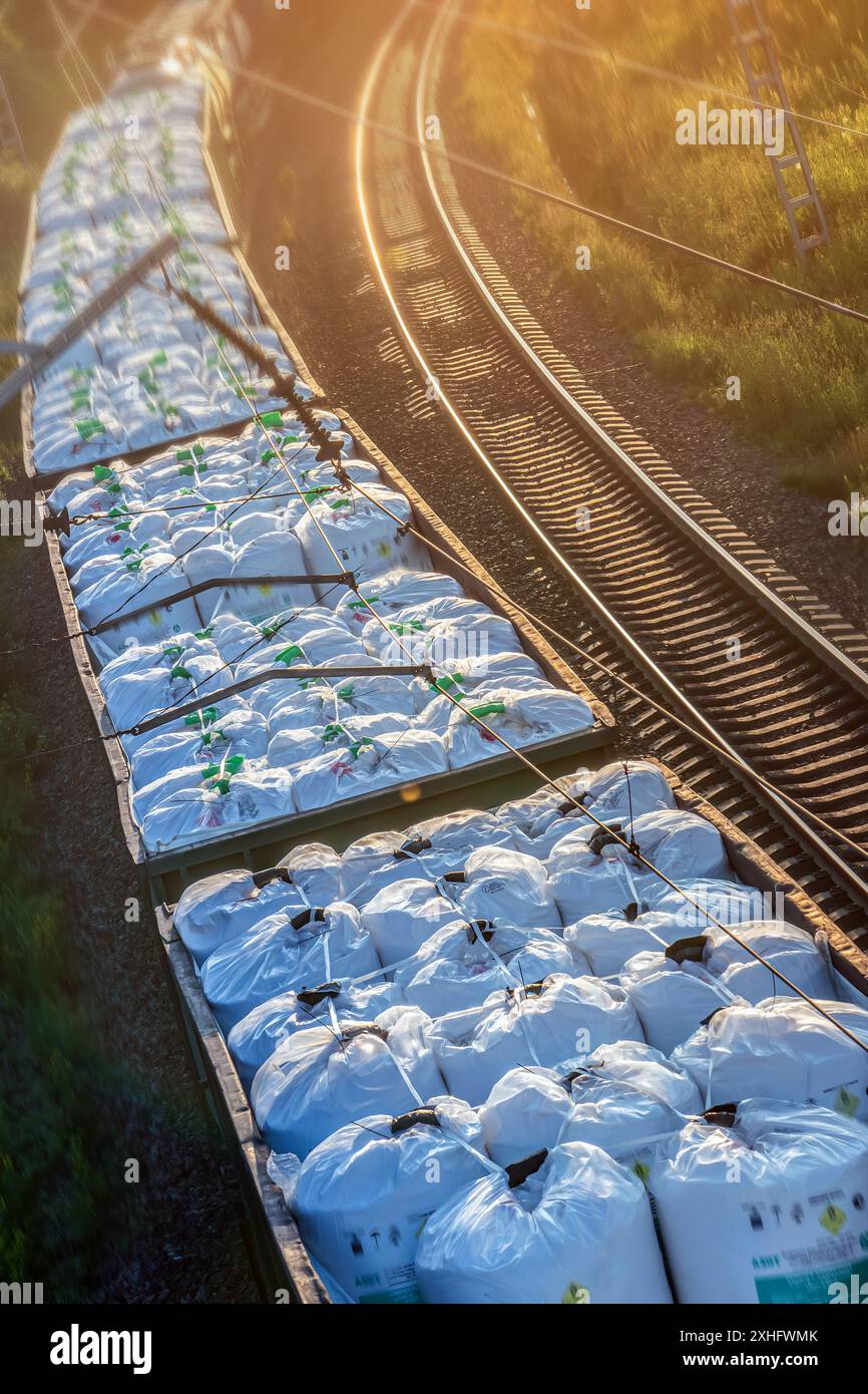 Un train de marchandises chargé de gros conteneurs circulant sur une voie ferrée au lever du soleil avec une lumière dorée. Banque D'Images