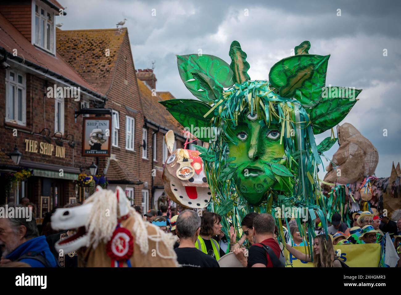 Folkestone, Kent, Royaume-Uni. 13 juillet 2024. Défilé annuel du Charivari Day. Folklore britannique et traditions rituelles sont le thème de la saisissante parade du carnaval de cette année. Des sculptures massives de tête ornent les épaules des jeunes locaux avec des enfants de l'école primaire à travers le district habillant aux couleurs du thème de l'année. Marchant du stade, en passant par la ville jusqu’au kiosque à musique Leas, le Charivari Day reste la plus grande tradition coutumière de Folkestone depuis 1997 et attire des centaines de spectateurs dans la ville portuaire en bord de mer. Crédit : Guy Corbishley/Alamy Live News Banque D'Images