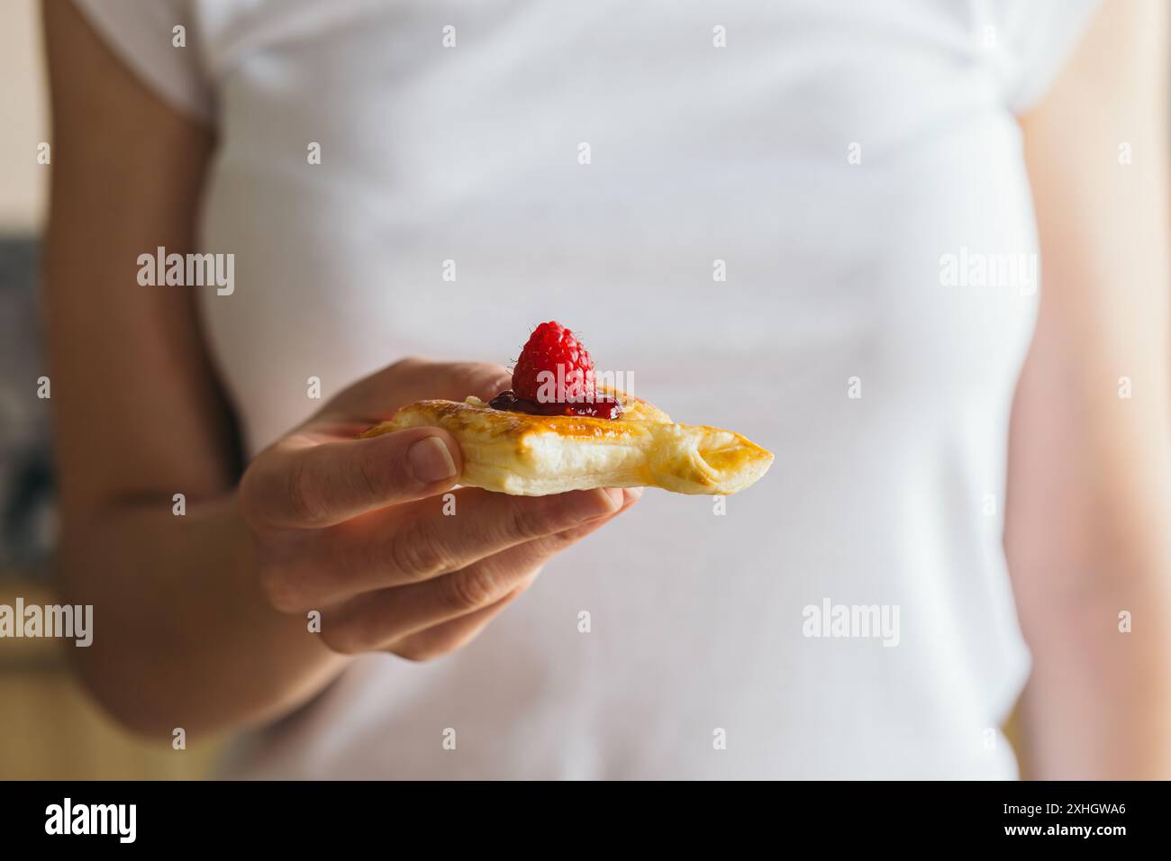 Gros plan de la main d'une femme tenant une petite pâte feuilletée remplie de camembert et de confiture de raspeberry décorer avec une framboise fraîche. Banque D'Images