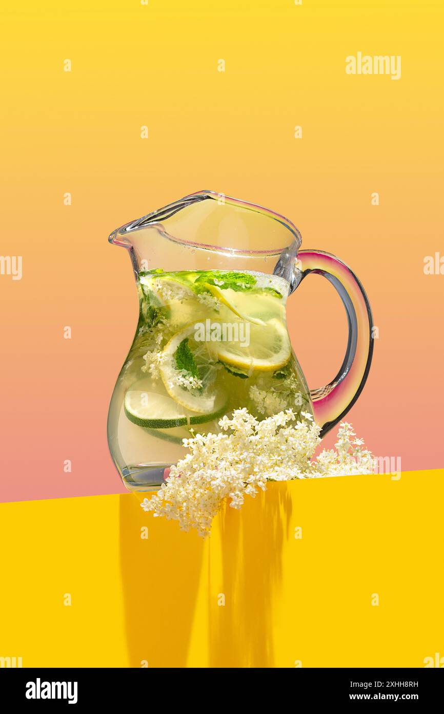 Limonade de fleurs de sureau fraîches maison garnie de zeste de citron et d'une branche en fleurs sur un fond rose et jaune vif Banque D'Images