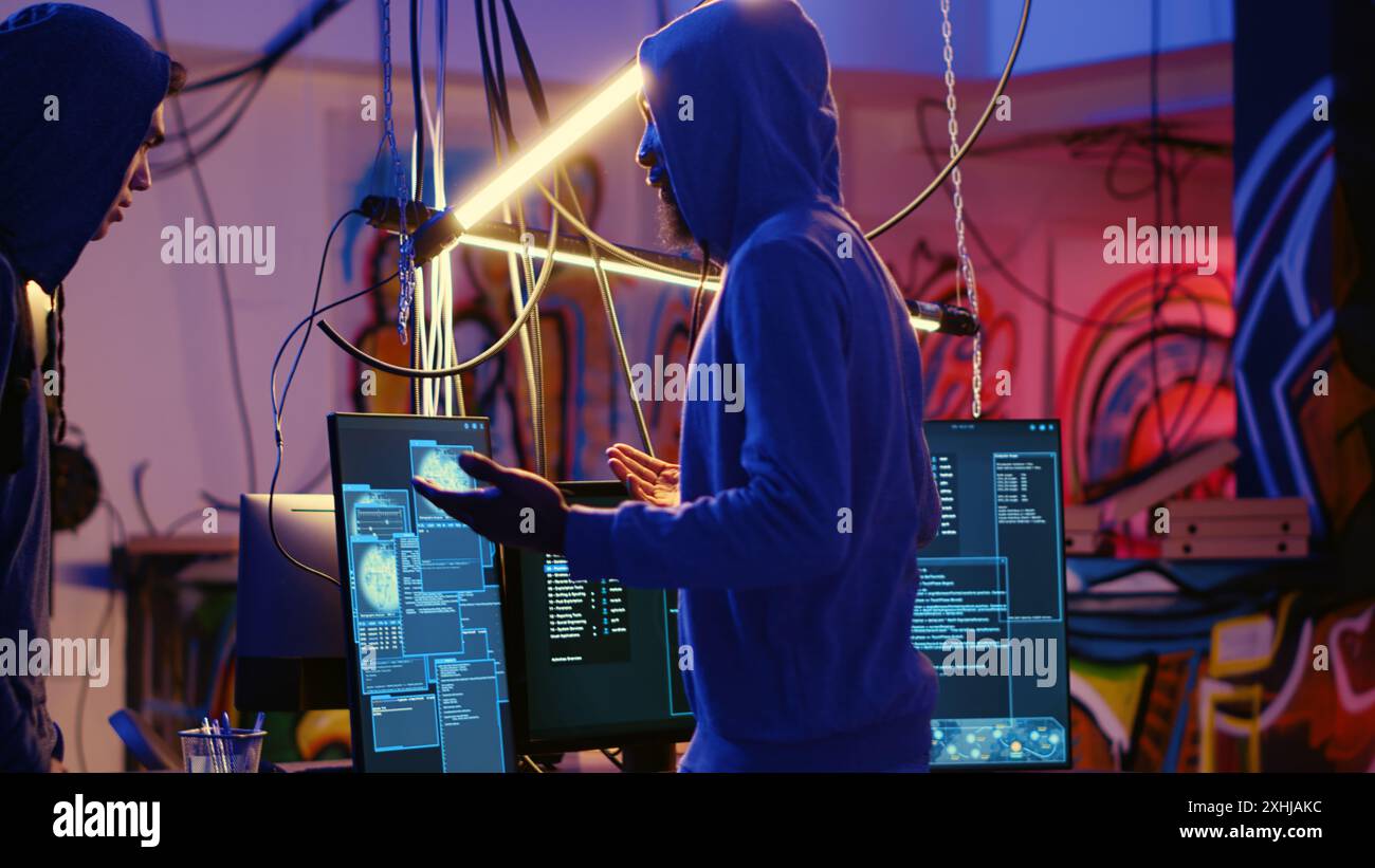 Chef de groupe de pirates informatiques voyous accueillant un nouveau membre dans une base souterraine cachée, prêt à lui apprendre comment passer les mesures anti-sabotage mises en œuvre par les entreprises pour protéger leurs produits Banque D'Images