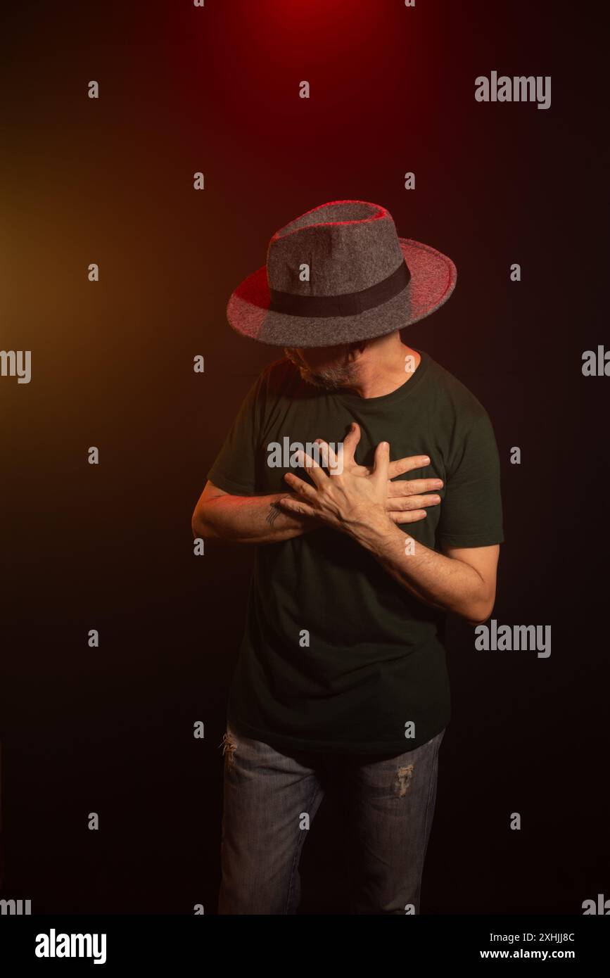 Homme mystérieux portant un chapeau debout posant pour la photo. Portrait de studio. Fond rouge foncé avec fumée artificielle. Banque D'Images