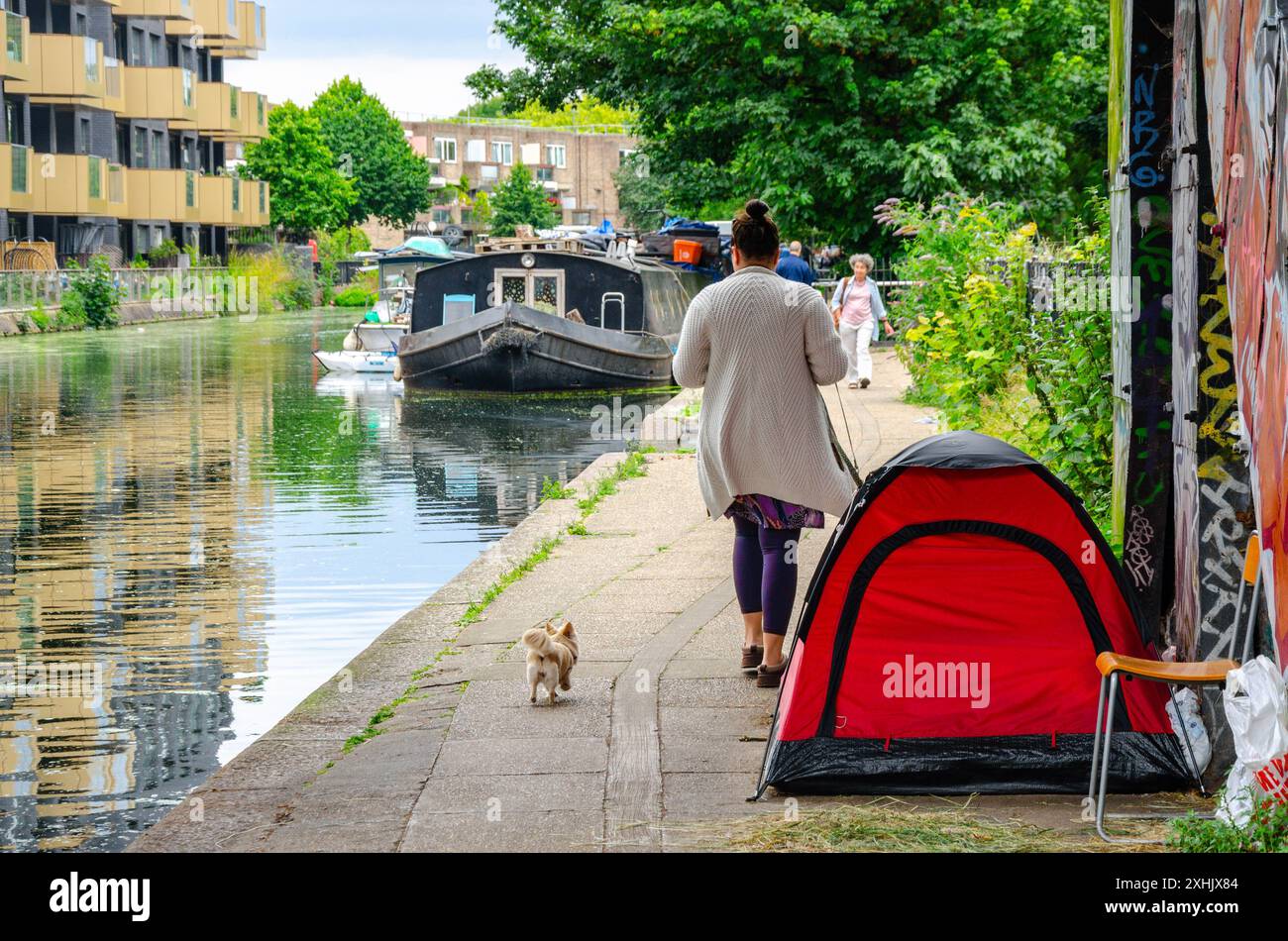 Une dame promène son chien devant une tente dressée sous un pont sur le chemin le long du bras de Paddington du Grand Union canal à Londres, au Royaume-Uni Banque D'Images