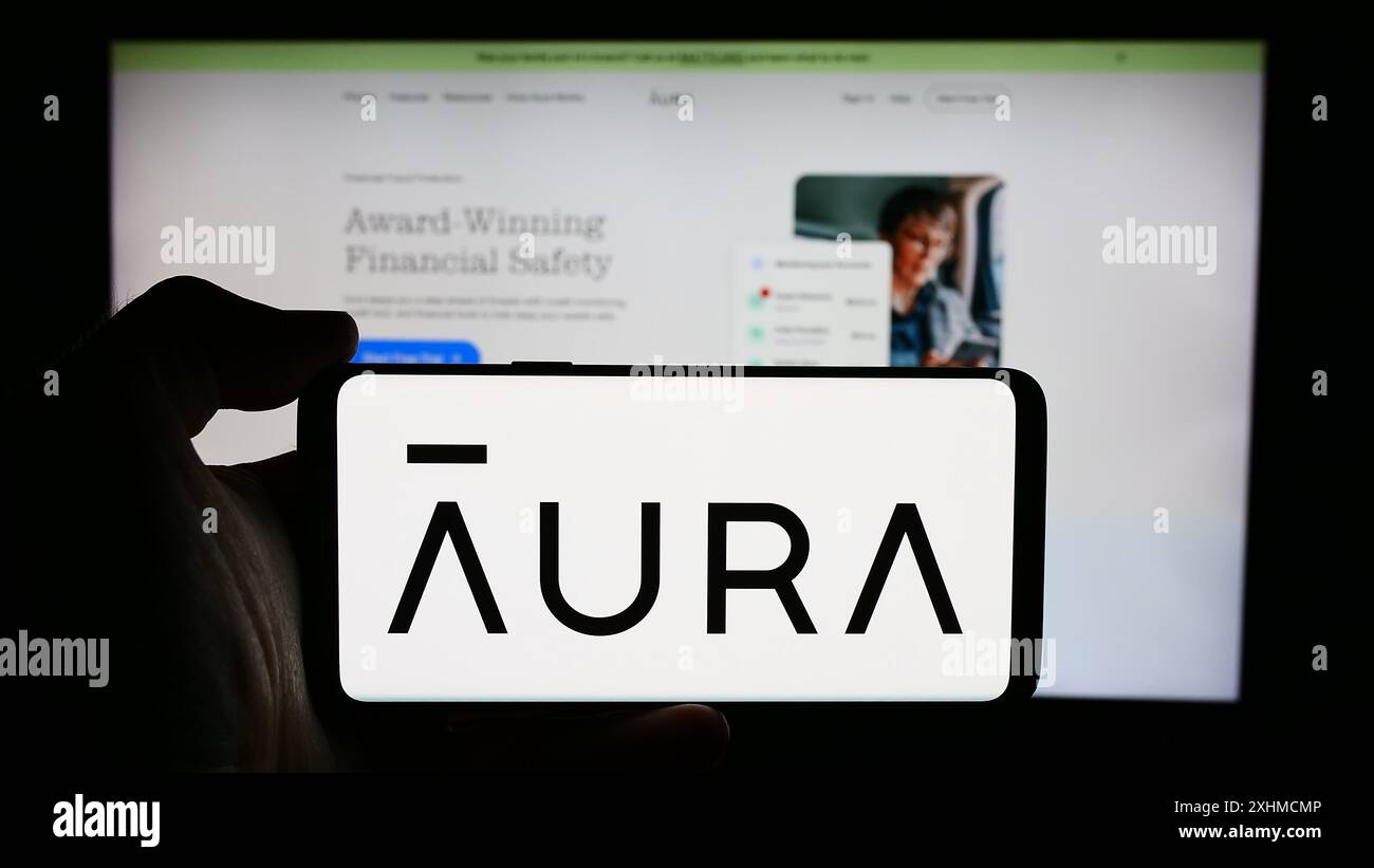 Personne tenant un téléphone portable avec le logo de la société américaine de logiciels de cybersécurité aura Sub LLC en face de la page Web de l'entreprise. Concentrez-vous sur l'affichage du téléphone. Banque D'Images