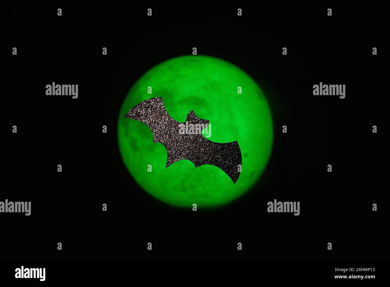 Chauve-souris en papier scintillant sur un fond de lune vert. Artisanat minimaliste d'Halloween Banque D'Images