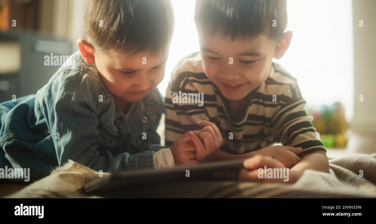 Portrait de deux enfants asiatiques masculins utilisant une tablette numérique pendant le week-end dans leur chambre. Deux adorables frères et sœurs regardant leur spectacle d'enfants préférés. Concept d'enfance, innocence et nostalgie Banque D'Images