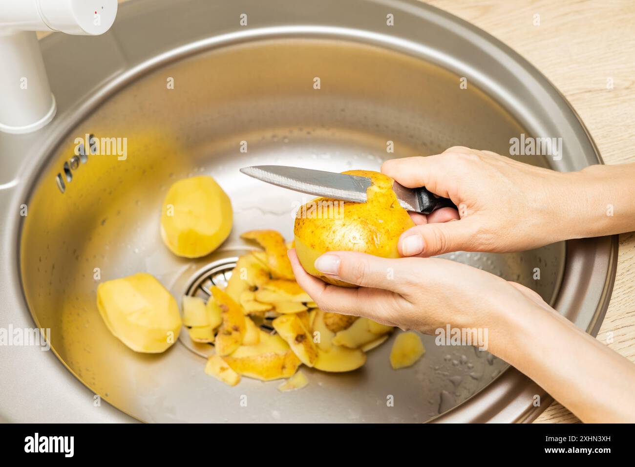 femme au foyer épluche les pommes de terre fraîches avec un couteau dans la cuisine. l'homme épluche les pommes de terre avec un couteau dans l'évier de la cuisine. épluchez les peaux de pommes de terre. épluchez la pota Banque D'Images