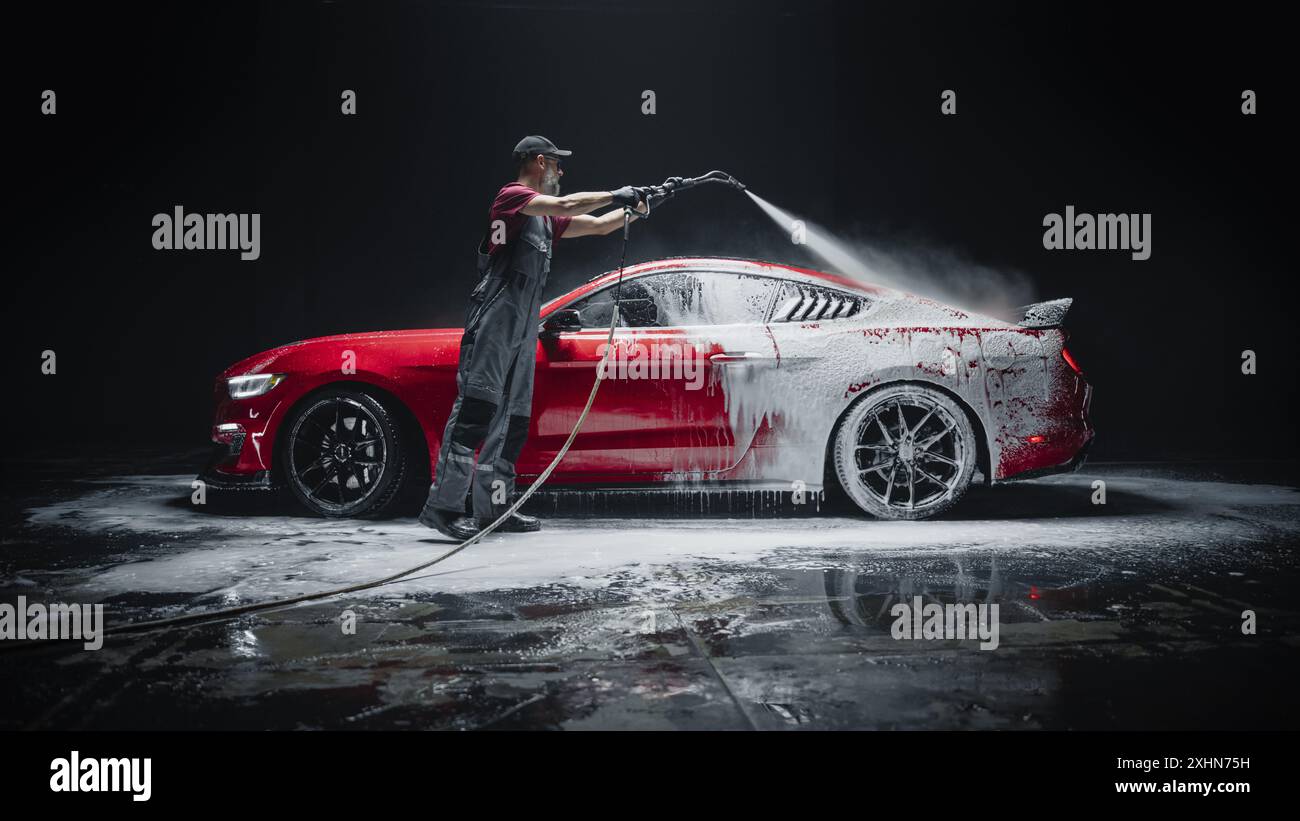 Détaillant automobile lavant le savon intelligent et la mousse avec un nettoyeur haute pression à l'eau. Gros plan d'une voiture de performance rouge soignée dans un atelier d'entretien de véhicules professionnels Banque D'Images