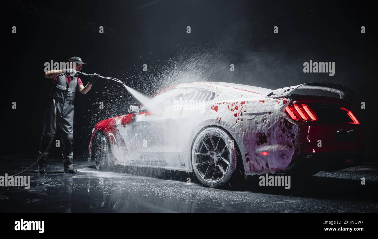 Détaillant automobile lavant le savon intelligent et la mousse avec un nettoyeur haute pression à l'eau. Red performance car obtenir des soins et des soins dans un atelier d'esthétique de véhicules professionnels Banque D'Images