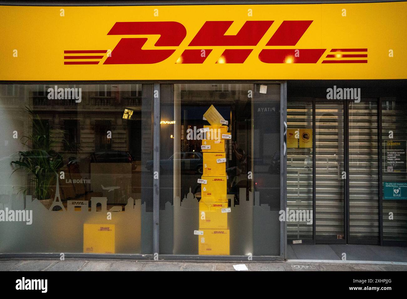 Paris, France - 14 juillet 2024 : un magasin DHL à Paris, fermé la nuit, avec des colis DHL empilés dans la vitrine *** Eine DHL-filiale à Paris, die in der Nacht geschlossen ist, mit gestapelten DHL-Paketen im Schaufenster Banque D'Images